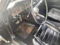 Interior view of a 1966 Ford Mustang showing a black leather seat steering wheel and dashboard with round gauges and a shiny metal gear shift