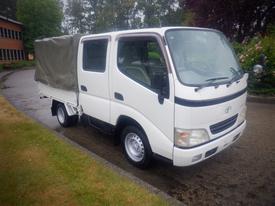 A white 2003 Toyota Toyoace with a covered cargo bed parked on a rain-soaked road