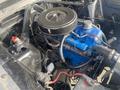 Engine compartment of a 1966 Ford Mustang featuring a blue engine block with black air filter and various hoses and components visible
