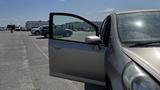 A silver 2006 Honda Fit with an open driver side door parked on a pavement with water droplets on the window