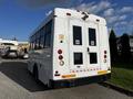 A white 2015 Chevrolet Express bus viewed from the rear featuring large windows and two rear doors with a circular emblem on them