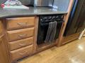 A kitchen area featuring a black oven with five burners a towel hanging on the handle and wooden cabinets below a countertop