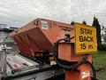 A Swenson spreader mounted on the back of a 2009 Ford F-550 with an orange hopper and a yellow sign that reads STAY BACK 15 m