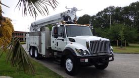 A 2012 International 7400 service truck with a white body and a hydraulic lift system mounted on the bed