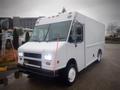 A 2003 Freightliner MT45 Chassis with a white exterior and sliding side door its headlights are illuminated and it features a flat front end design