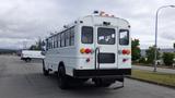 A white 2015 International PC105 bus with multiple lights on top and a ladder on the back parked on a street