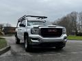 A white 2018 GMC Sierra 1500 pickup truck with a black grille and roof rack positioned at an angle on a driveway