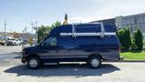 A blue 2013 Ford Econoline van with a raised roof and a ladder rack on top parked on a paved surface