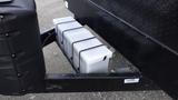 A series of three white storage containers secured with black straps attached to the underside of a trailer hitch