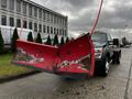 A 2012 Ford F-550 truck with a large red snow plow attached to the front featuring visible wear and tear