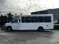 A white 2015 Chevrolet Express shuttle bus with large windows and a high roof is parked on a street