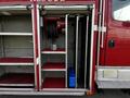 A red 1994 Freightliner FL80 with open storage compartments showcasing equipment like a hose reel and shelves for firefighting gear