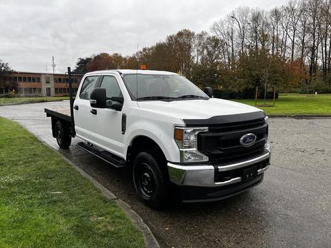 A 2020 Ford F-350 SD in white with a black front bumper and a flatbed configuration parked on a road