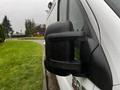 Close-up of the side mirror of a white 2018 RAM Promaster van showcasing a sleek design with a textured black finish and droplets of rain on its surface