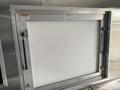 A stainless steel service window frame designed for a food truck with a warning label inside the frame