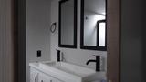 A modern bathroom sink with a white countertop and two black-framed mirrors above it, featuring a black faucet and neatly arranged towels on the counter