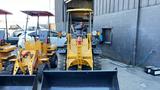 A yellow 2024 AGT BH50G compact loader with a front loader attachment and large tires positioned in front of a building