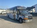 A 2017 Chevrolet Express bus with an open front door and a partially exposed interior, showing seating and a driver's area