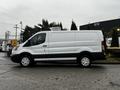 A white 2016 Ford Transit cargo van with a sliding door and silver wheels parked alongside palm trees