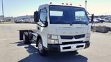 A 2015 Mitsubishi Fuso FE truck with a flatbed chassis and amber lights on the roof parked in an open area