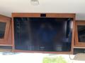 A Samsung flat-screen television mounted on the wall of a Class A motorhome with wooden cabinetry on either side