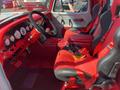 Interior of a 1962 Ford F-100 featuring red and black bucket seats a racing steering wheel and multiple gauges on the dashboard