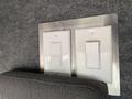 Two light switch plates in a food truck interior mounted on a metal panel with a gray fabric cushion in the foreground