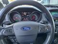 The steering wheel of a 2018 Ford Focus with controls for audio and cruise, featuring the Ford logo and dashboard displays behind it