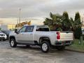 A 2023 Chevrolet Silverado 3500HD in silver with a crew cab and chrome accents parked in a lot with palm trees nearby