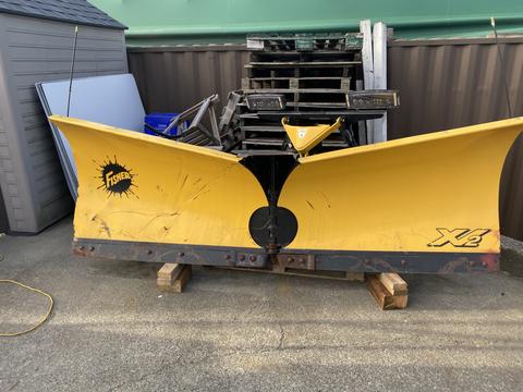 A yellow Fisher XV2 snow plow blade resting on wooden pallets with a black mounting plate in the center