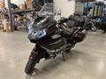 A 2013 BMW K1600GTL motorcycle with a maroon body and black leather seat featuring a large windshield and sleek design