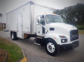 A white 2021 Mack MD box truck with a large cargo area and orange lights on the roof parked with the driver's side facing forward