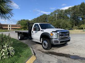 A 2013 Ford F-450 SD pickup truck with a flatbed design in white color parked on a paved area