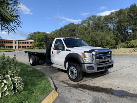 A 2013 Ford F-450 SD pickup truck with a flatbed design in white color parked on a paved area