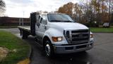 A white 2008 Ford F-650 flatbed truck with a prominent grille and multiple orange lights on the roof facing slightly to the right