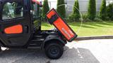 A 2018 Kubota RTV X1100C utility vehicle with a dump bed raised displaying its orange and black exterior design