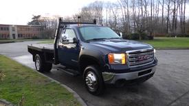 A 2011 GMC Sierra 3500HD pickup truck with a flatbed design and chrome wheels parked on a driveway