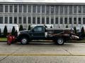 A 2012 Ford F-550 with a snowplow attachment and a flatbed is parked along a street