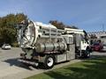 A white 2013 International 7400 vacuum truck with a large cylindrical tank and multiple hoses attached at the rear