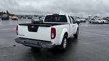 A white 2016 Nissan Frontier pickup truck is parked with its tailgate down and black bed liner visible