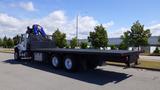 A 2017 Freightliner M2 106 flatbed truck with a blue loading arm attached is parked on a street