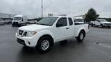 A white 2016 Nissan Frontier parked at an angle with a four-door cab and a short bed showcasing its sleek design and chrome accents