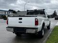 A white 2011 Ford F-250 SD pickup truck is parked with a truck bed cover and a metal rack on the back. The truck has large tires and a robust build