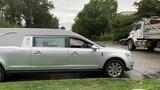 A silver 2013 Lincoln MKT hearse with a sleek design and elongated body parked on the side of a road