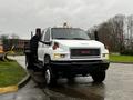 A 2005 GMC C5 Duramax truck with a white body black dump bed and yellow warning light on the roof parked on a wet surface