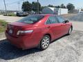 A red 2007 Toyota Camry Hybrid parked on gravel with a visible rear and side profile, featuring alloy wheels and a sleek design