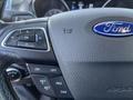 Close-up of a steering wheel with Ford branding and control buttons for settings, audio, and cruise control