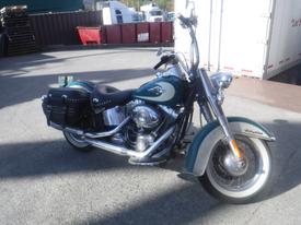 A 2009 Harley-Davidson FLSTC motorcycle with a teal and chrome finish features a black seat and a leather saddlebag adorned with studs