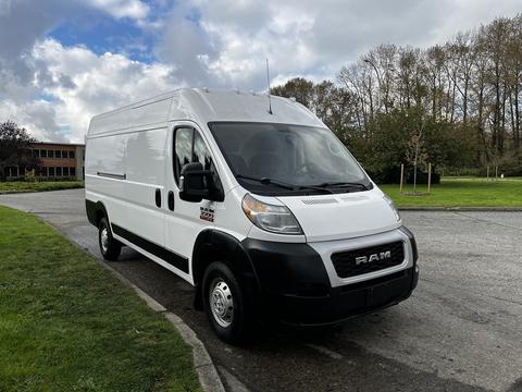 A 2019 RAM Promaster van with a white exterior parked on a street viewed from the front and slightly to the side