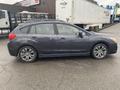 A 2014 Subaru Impreza in gray is parked with its side view visible showcasing its compact hatchback design and alloy wheels